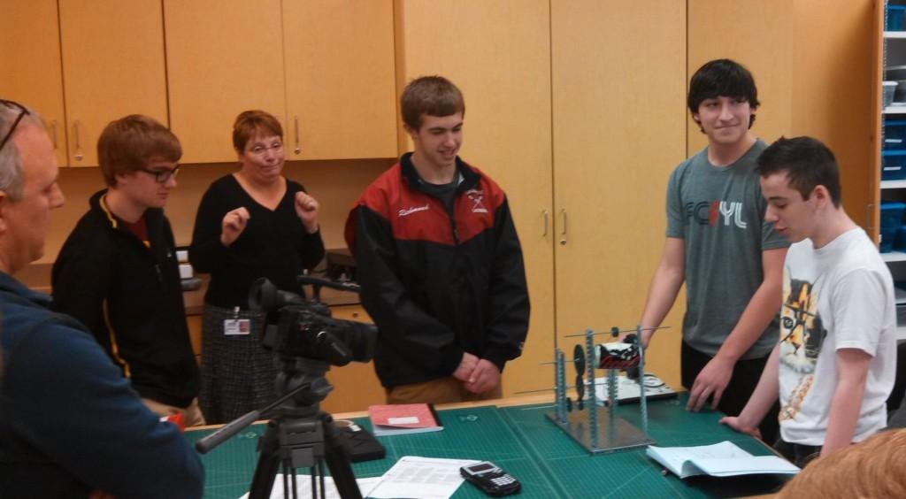 PLTW instructor Patrick Greene films students Justin Richmond, Will Eckard, and David Wynne as they present a machine that they built to lift a soda can.