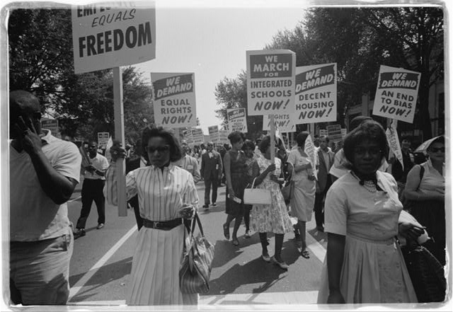 A procession of African Americans carry signs for equal rights, integrated schools, decent housing, and an end to bias.