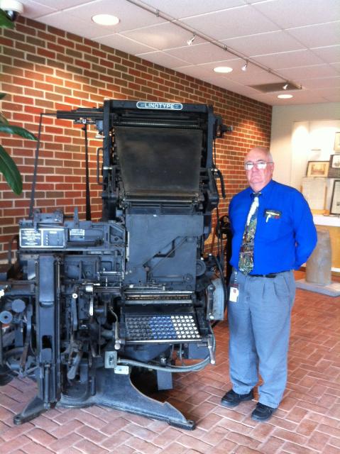 Ed Waters stands in front of the Linotype printing press.