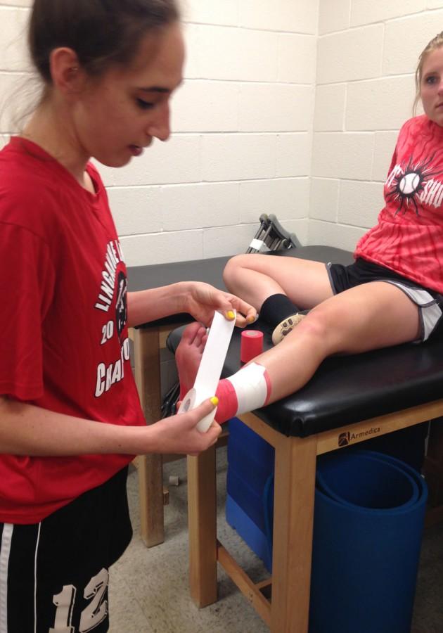 Caroline tapes up softball player Shylo Arneson before practice.