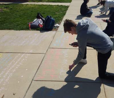 Senior JD Ensor writes The New Colossus by Emma Lazarus for NEHS Poetry on the Sidewalk activity.
