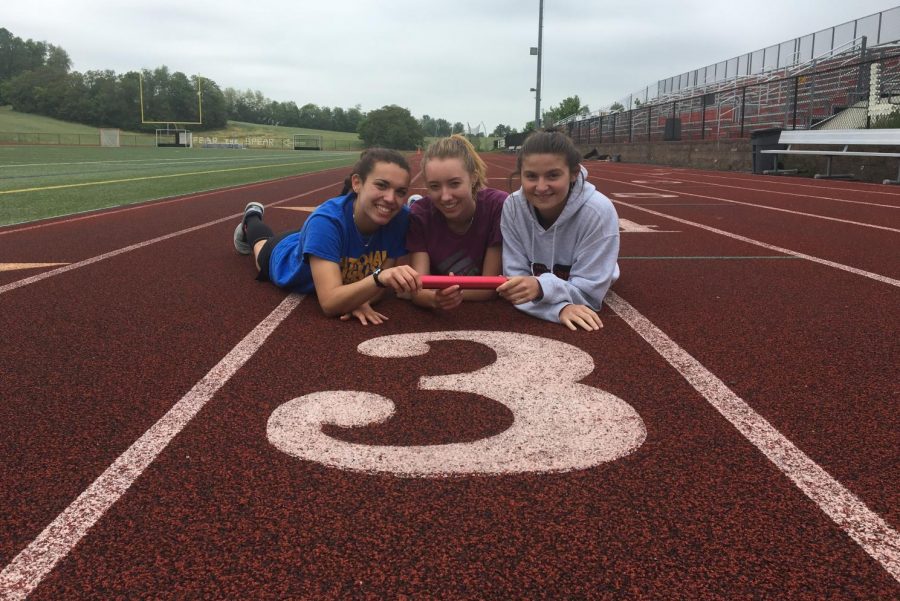 Seniors Morgan Matthews, Khelsa Connolly, and Savannah Sitler pose in front of lane three on the track with their relay baton.