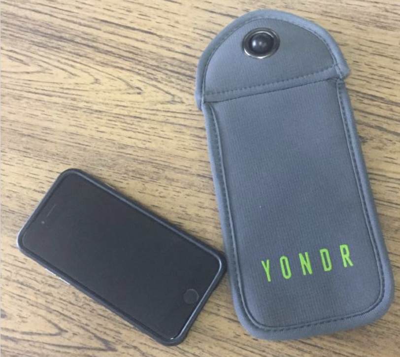 in this photo there is a Yondr pouch next to a phone, to show what the bag is for.