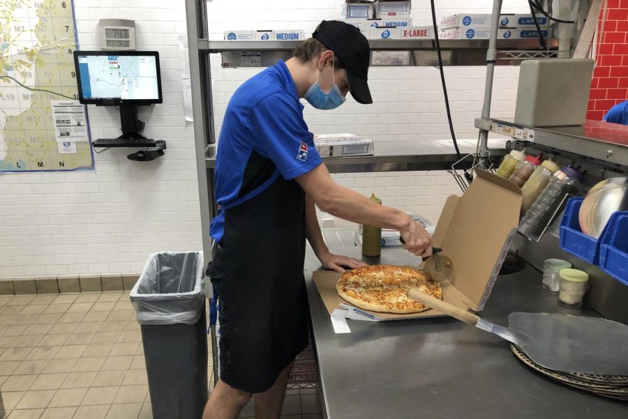 Braden Weinel cuts a pizza at work while wearing a face mask during the Covid-19 outbreak.