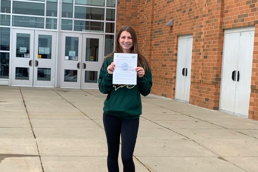 Madyson holding National Letter of Intent in front of Linganore's gymnasium. 