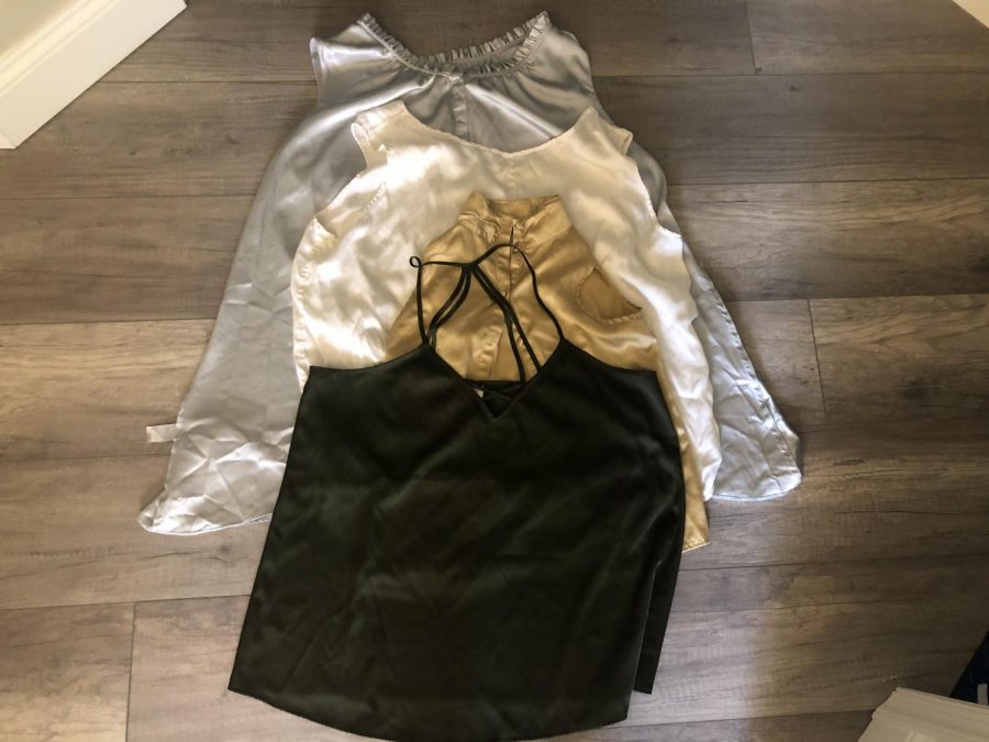 Spread of clothing from her last thrifting outing. She plans to take these old silk tops and make cute and trendy tank tops. She is going to trim them up and sew matching colors together to create new tops.