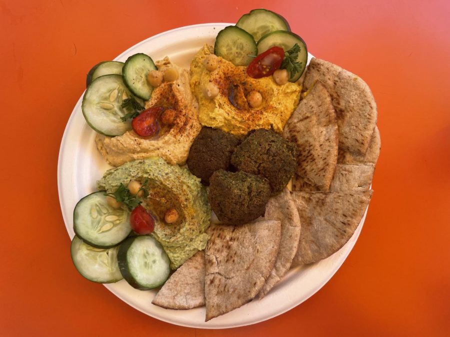 The Hippy Sampler from Hippy Chick Hummus comes with spicy pumpkin hummus, Old Bay hummus, and spinach Pesto hummus. It is accompanied by falafel and pita bread slices.