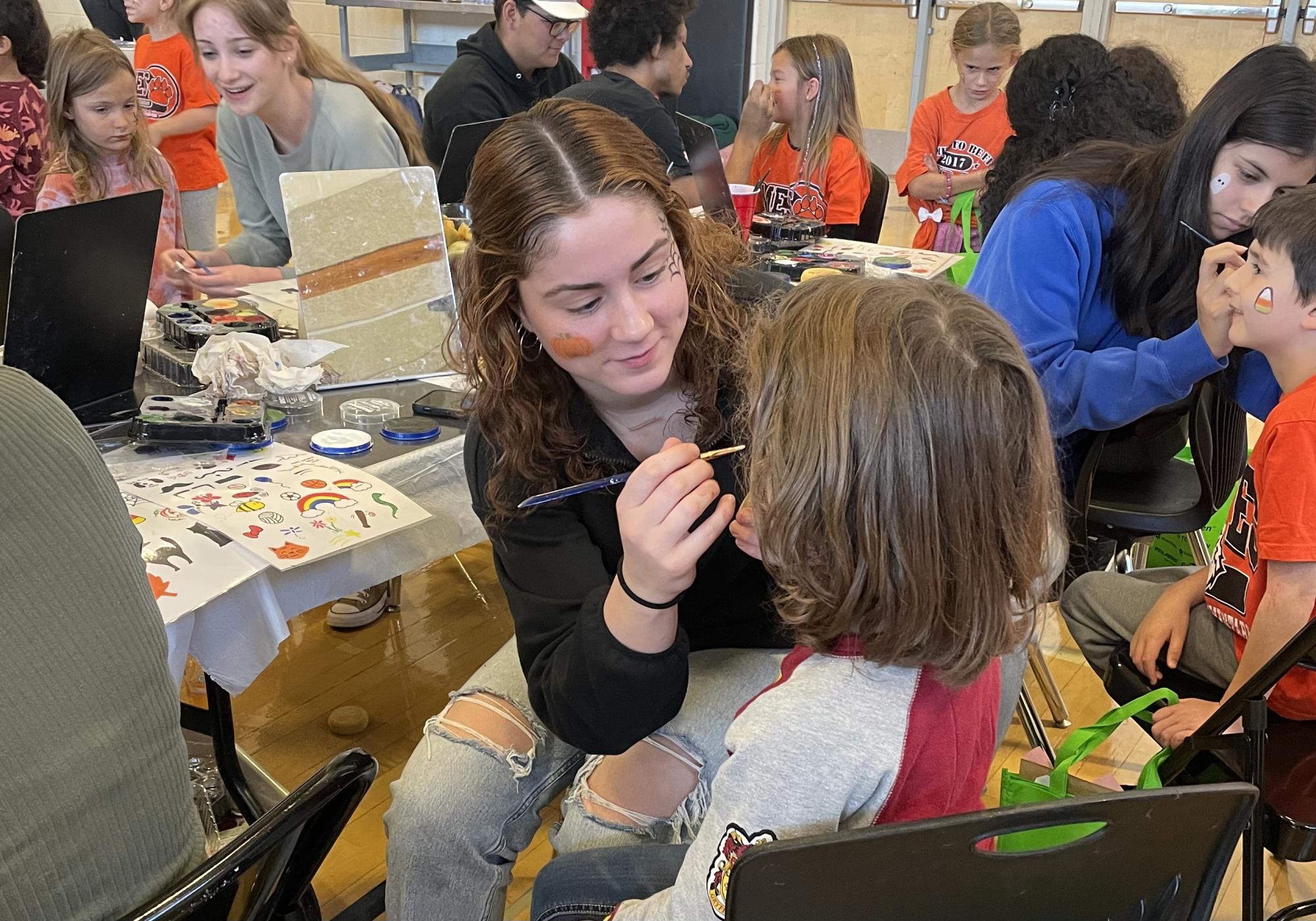 Junior Genevieve Vlha paints a childs face at the face paint booth at the community show.