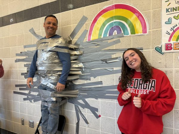 Senior Chloe Little poses alongside Principal Dillman during third lunch, as students complete taping him to the wall.