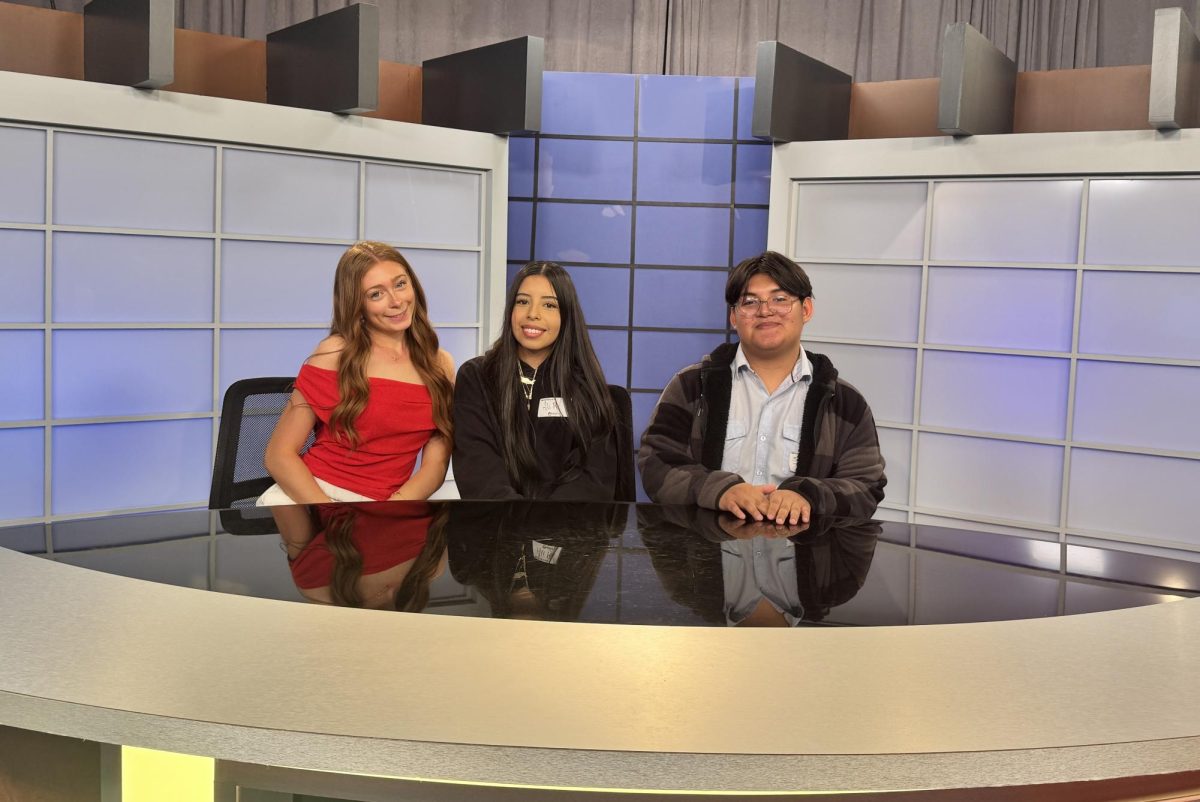 Rory McMillin, Alison Ramos and Jeremias Romero-Ramirez sit at the anchor desk on their tour of University of Maryland's broadcast studio.